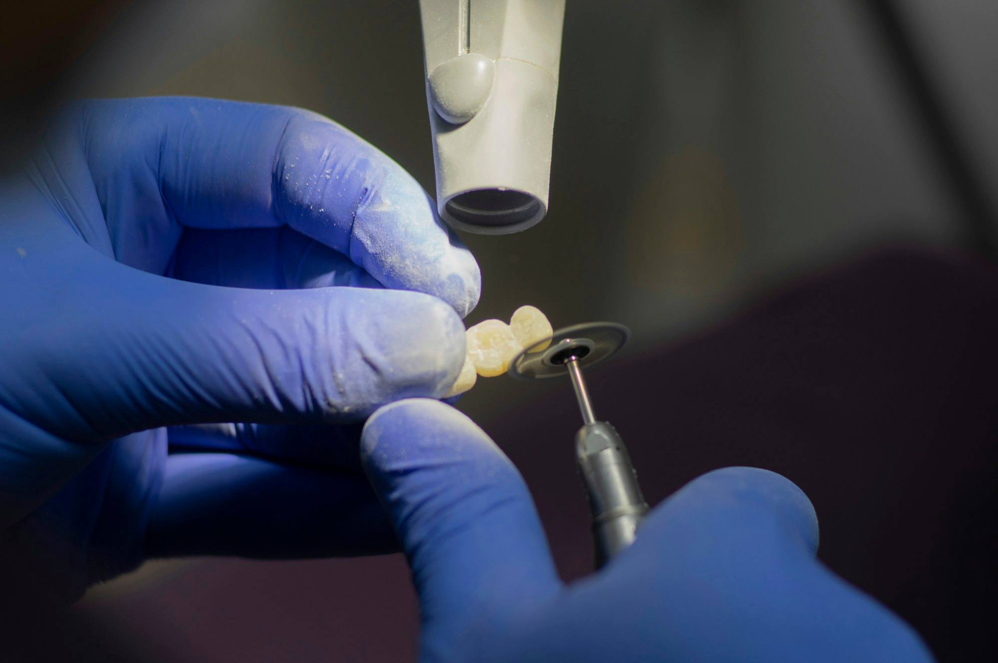 Manos con guantes trabajando una pieza dental con una pieza de mano